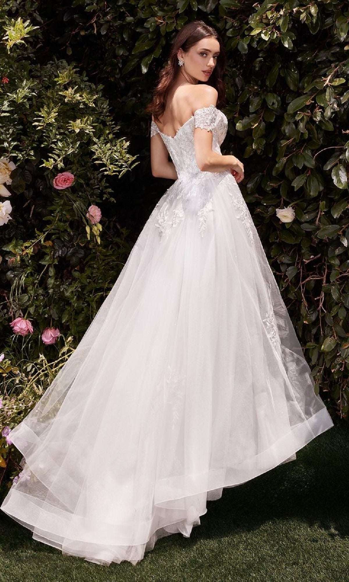 A woman wearing the affordable Ladivine C159W Off-White Long Wedding Dress stands outdoors on grass, surrounded by greenery and flowers.